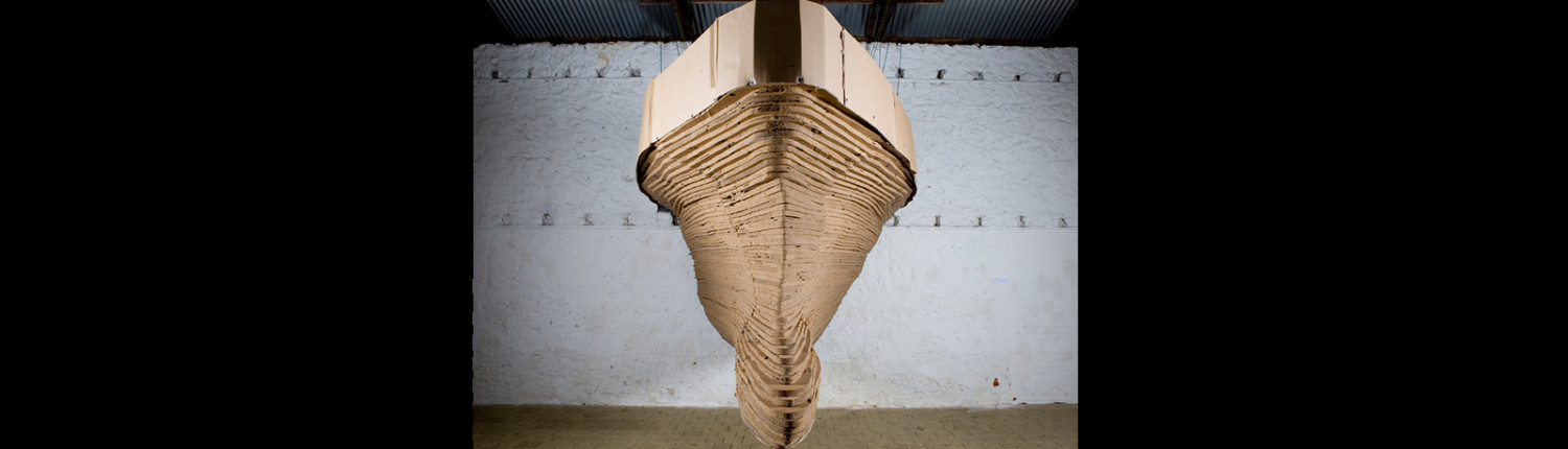 A boat made out of cardboard is hanging in the ceiling.