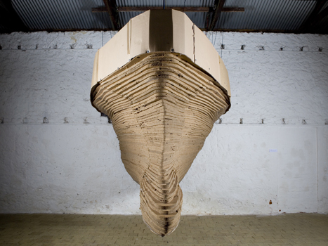 A boat made out of cardboard is suspended in the air.
