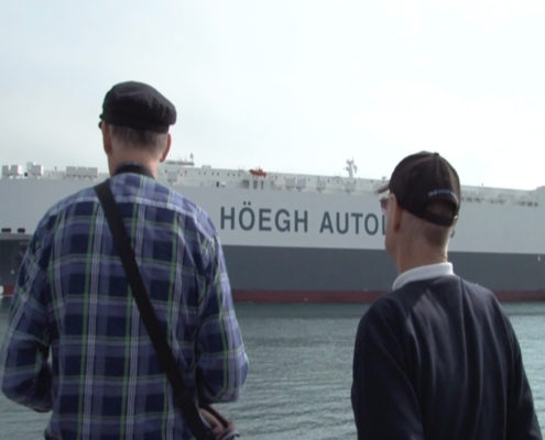 Two men standing in front of a large ship.