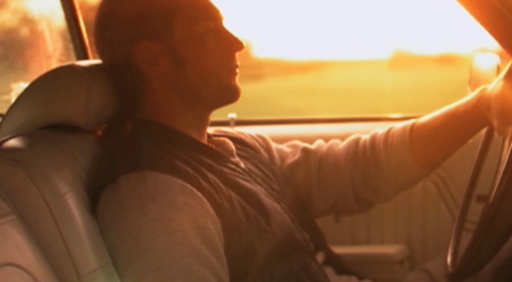 A man sitting in the back of a car looking out at the sunset.